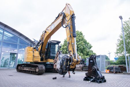 Bagger, der bei einem Abbruchprojekt vor einem Gebäude Baumaterialien aufhebt.