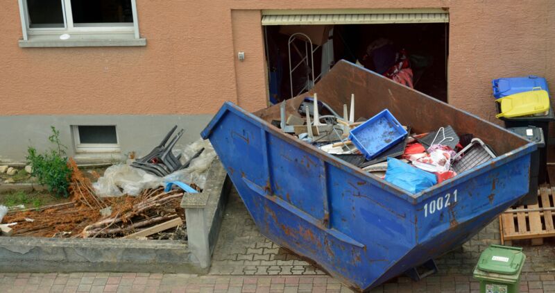Ein Container mit Bauschutt und Sperrmüll steht für eine Entrümpelung vor einem Haus.