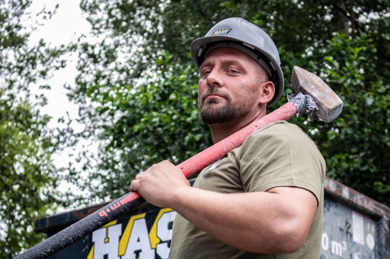 Ein entschlossen aussehender Mitarbeiter mit Vorschlaghammer und Container im Hintergrund