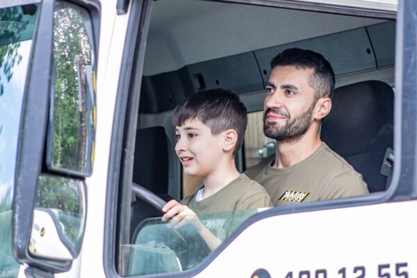 Ein Vater zeigt seinem Sohn, wie das Führerhaus eines Lkw aussieht und lässt ihn lenken.