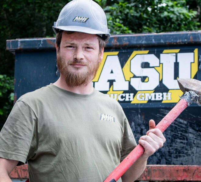 Ein Mitarbeiter steht mit Helm und Hammer vor einem Container von HASU Abbruch