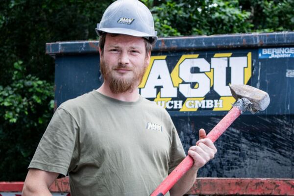 Ein Mitarbeiter steht mit Helm und Hammer vor einem Container von HASU Abbruch